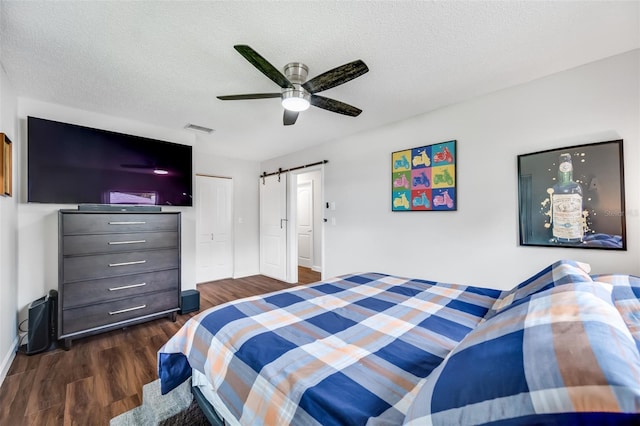 bedroom featuring a textured ceiling, dark hardwood / wood-style floors, a closet, ceiling fan, and a barn door