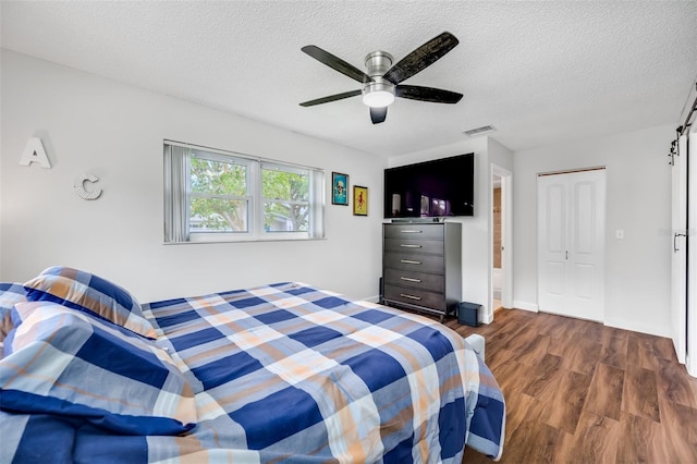 bedroom with a barn door, ceiling fan, a closet, dark wood-type flooring, and a textured ceiling