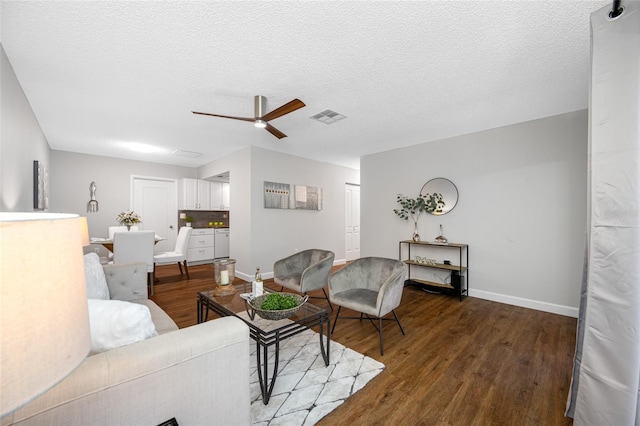 living area featuring visible vents, baseboards, a textured ceiling, and wood finished floors