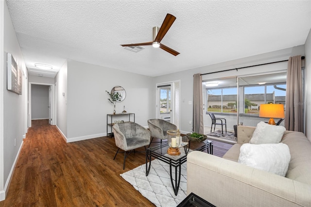 living room with visible vents, a textured ceiling, wood finished floors, baseboards, and ceiling fan