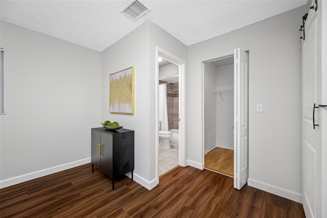 bedroom with baseboards, visible vents, dark wood-type flooring, a textured ceiling, and a barn door