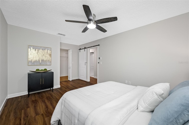 bedroom with visible vents, a barn door, wood finished floors, a textured ceiling, and a ceiling fan