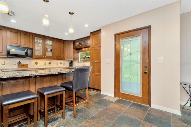 kitchen with hanging light fixtures, light stone counters, backsplash, and a kitchen bar