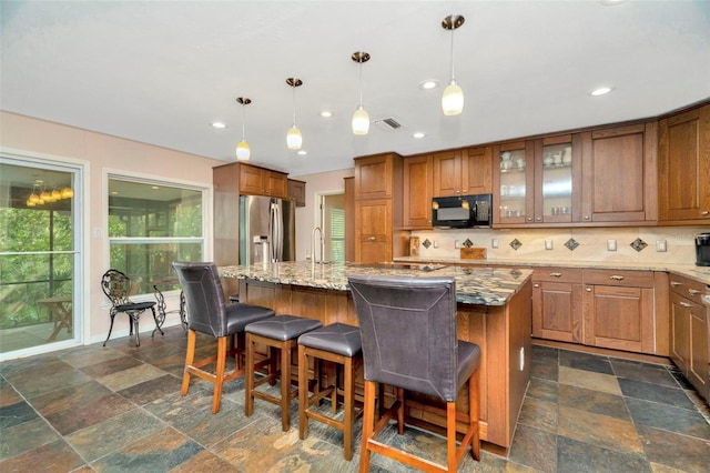 kitchen featuring a kitchen island with sink, stainless steel fridge with ice dispenser, a kitchen bar, and backsplash