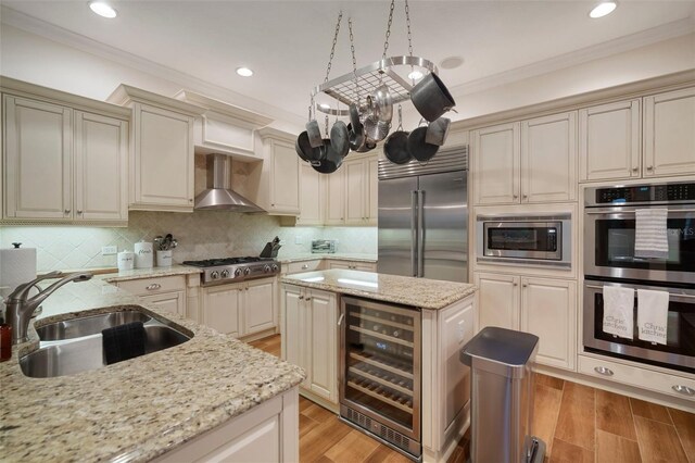 825 Islebay Dr, Apollo Beach, FL 33572 - kitchen featuring cream cabinetry, wall chimney exhaust hood, a sink, beverage cooler, and built in appliances