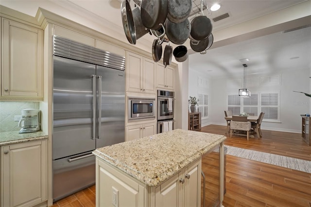 kitchen with built in appliances, light stone countertops, a center island, cream cabinetry, and light wood-type flooring