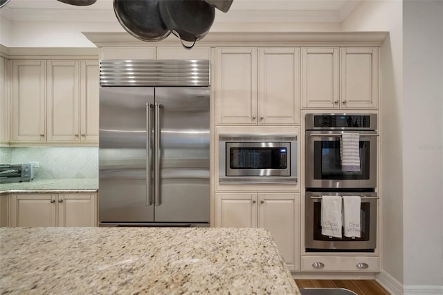 825 Islebay Dr, Apollo Beach, FL 33572 - kitchen with backsplash, built in appliances, wood finished floors, cream cabinets, and ornamental molding