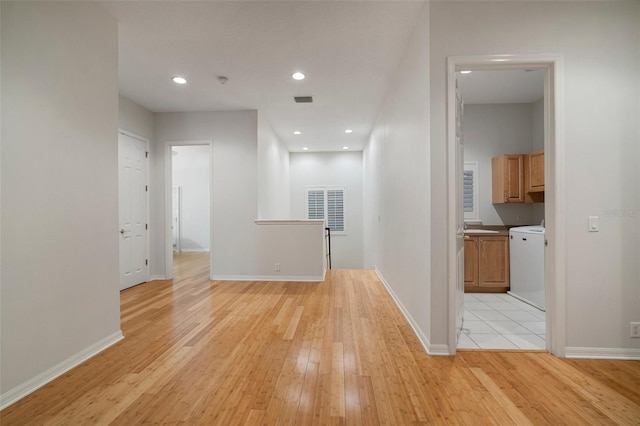 hall with light wood-type flooring, washer / dryer, and sink