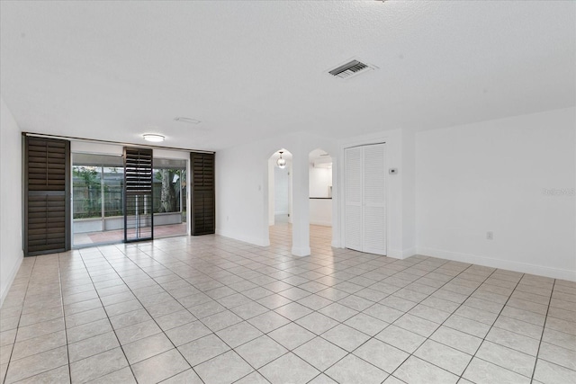 empty room with light tile patterned floors, visible vents, arched walkways, baseboards, and a textured ceiling