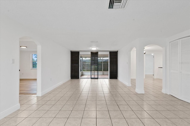 empty room featuring light tile patterned floors, arched walkways, visible vents, and baseboards