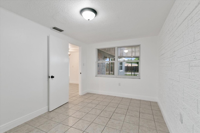 unfurnished room with a textured ceiling, light tile patterned floors, visible vents, and baseboards