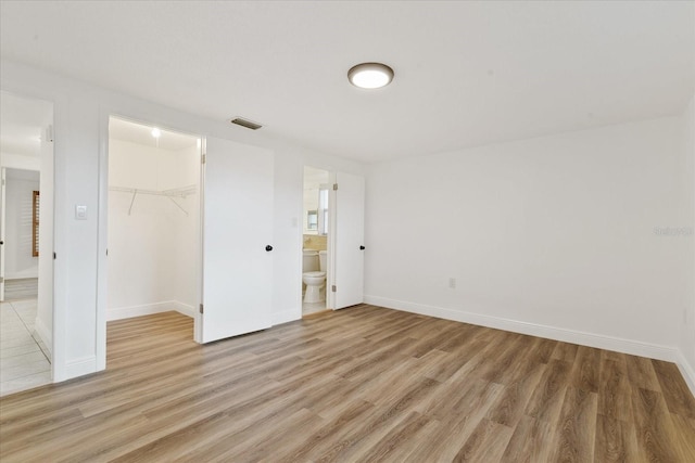 unfurnished bedroom featuring light wood-type flooring, a closet, visible vents, and a walk in closet