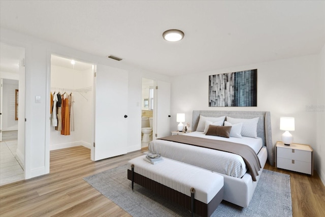 bedroom with light wood finished floors, visible vents, a walk in closet, and a closet