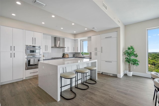 kitchen with a kitchen island, a kitchen breakfast bar, dark hardwood / wood-style floors, wall chimney exhaust hood, and white cabinets