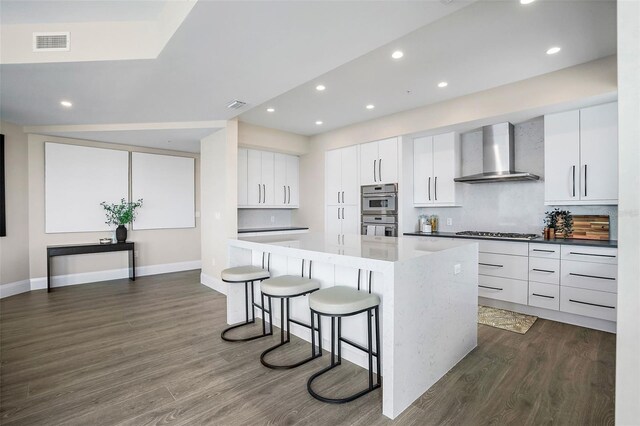 kitchen with a kitchen island, dark hardwood / wood-style flooring, stainless steel appliances, wall chimney range hood, and white cabinets