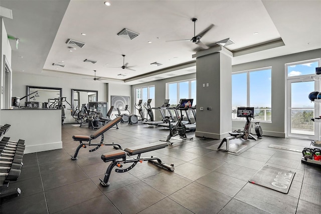 workout area with ceiling fan and a tray ceiling