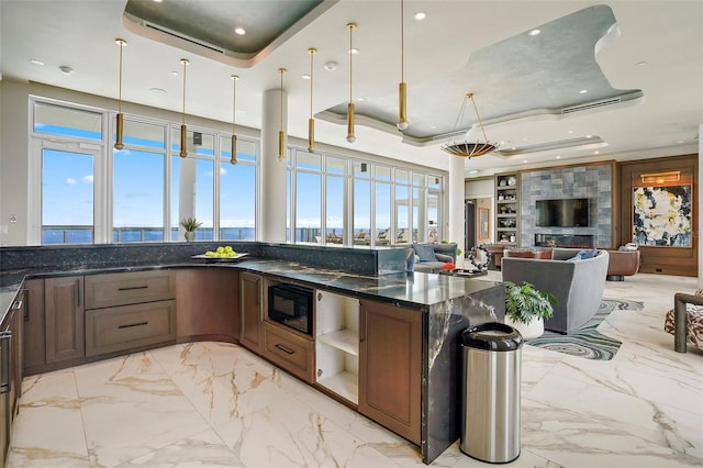 kitchen featuring dark stone countertops, a raised ceiling, a healthy amount of sunlight, and hanging light fixtures