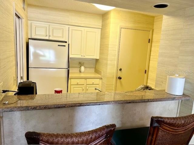 kitchen featuring stone counters, white refrigerator, white cabinetry, kitchen peninsula, and a kitchen bar