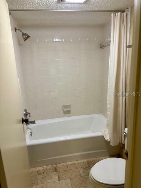 bathroom featuring toilet, shower / bath combination with curtain, and a textured ceiling