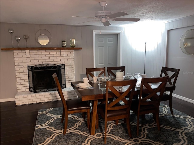 dining area featuring ceiling fan, dark wood-type flooring, a brick fireplace, wood walls, and a textured ceiling