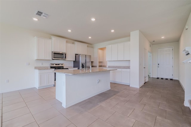 kitchen featuring a kitchen island with sink, white cabinetry, stainless steel appliances, light stone counters, and light tile patterned flooring