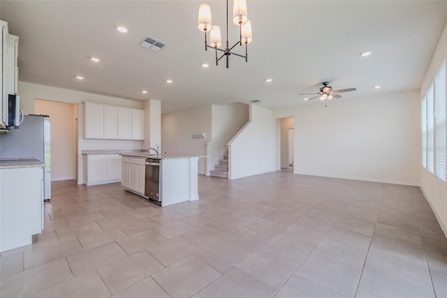 kitchen with pendant lighting, ceiling fan with notable chandelier, stainless steel appliances, a center island with sink, and white cabinets