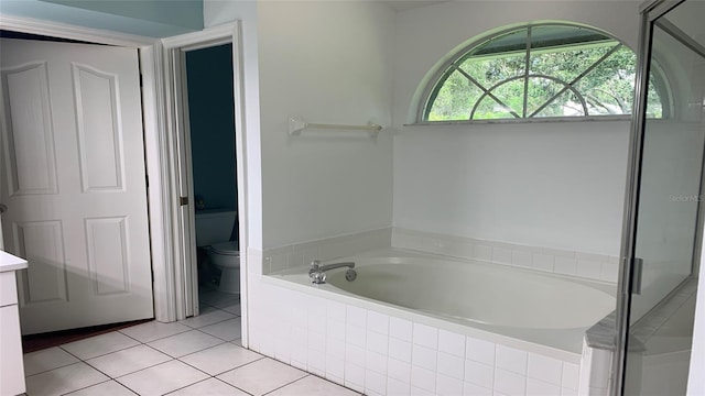 bathroom with tile patterned flooring, vanity, toilet, and a relaxing tiled tub