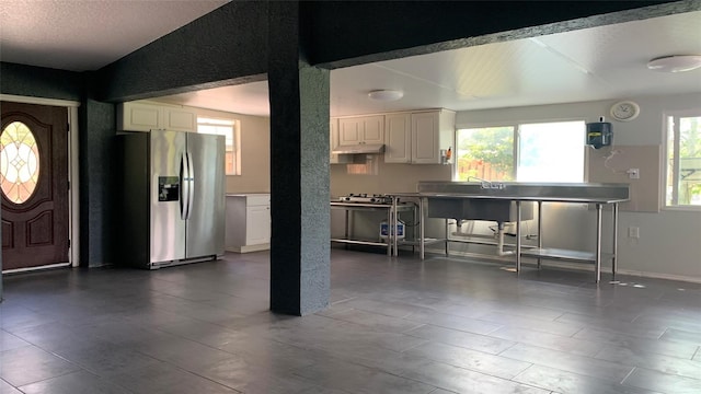 kitchen featuring stainless steel refrigerator with ice dispenser, vaulted ceiling, a textured ceiling, and white cabinets