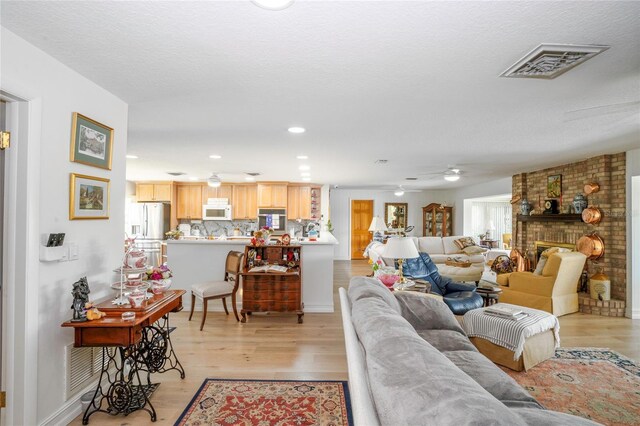 living room with light wood-type flooring, a textured ceiling, and a brick fireplace