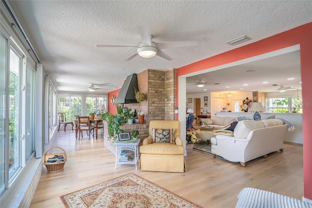 living room with a textured ceiling, a ceiling fan, visible vents, and light wood-type flooring