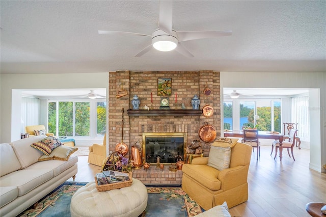 living room with a brick fireplace, a textured ceiling, ceiling fan, and wood finished floors