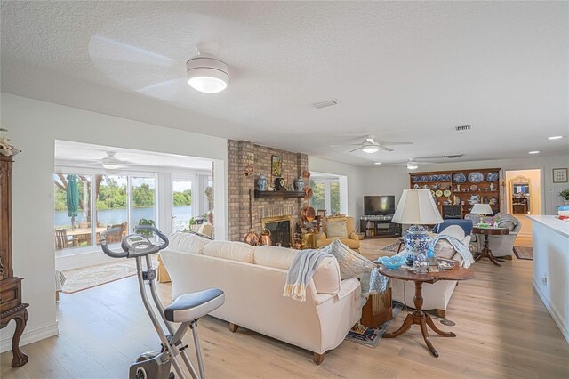 living room with light wood-type flooring, ceiling fan, a fireplace, and a textured ceiling