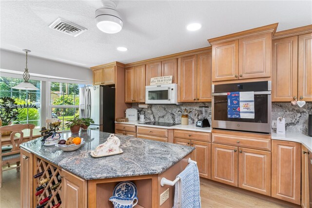 kitchen with a center island, light hardwood / wood-style flooring, appliances with stainless steel finishes, light stone countertops, and tasteful backsplash