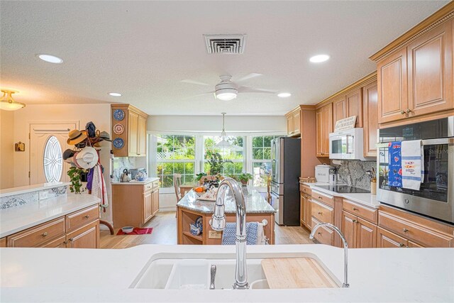 kitchen with a textured ceiling, light hardwood / wood-style flooring, stainless steel appliances, sink, and ceiling fan