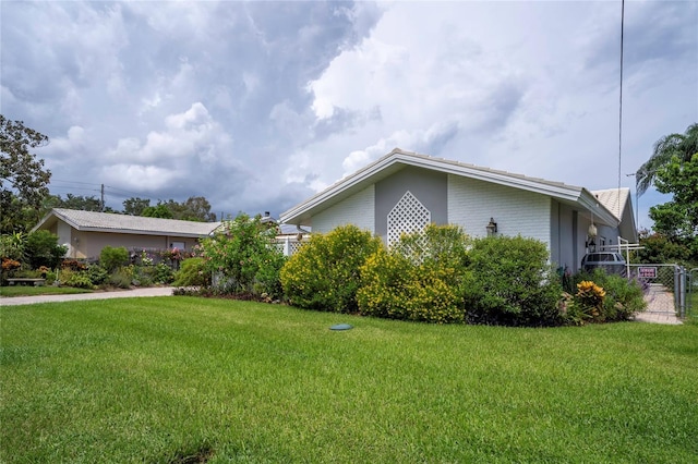 view of property exterior featuring brick siding, a lawn, and fence