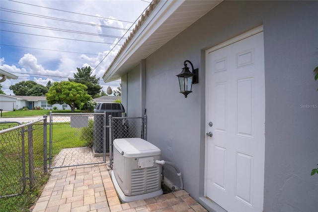 entrance to property featuring fence, stucco siding, cooling unit, a lawn, and a gate