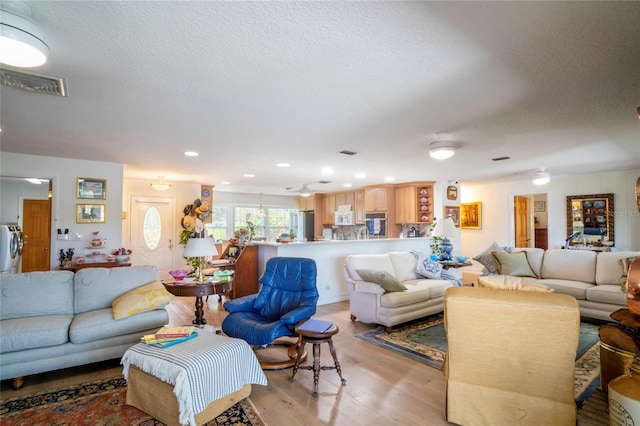 living room featuring visible vents, a textured ceiling, washer / dryer, and light wood finished floors