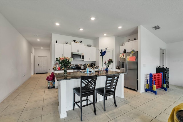 kitchen featuring white cabinets, a kitchen bar, a center island with sink, appliances with stainless steel finishes, and dark stone countertops