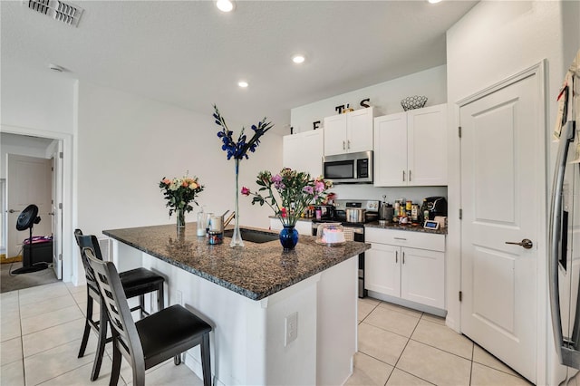 kitchen featuring dark stone countertops, a kitchen island with sink, stainless steel appliances, and white cabinetry