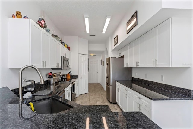 kitchen featuring sink, white cabinets, stainless steel appliances, and dark stone counters