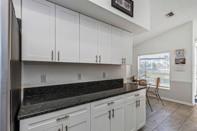 kitchen featuring lofted ceiling, white cabinets, and dark stone counters