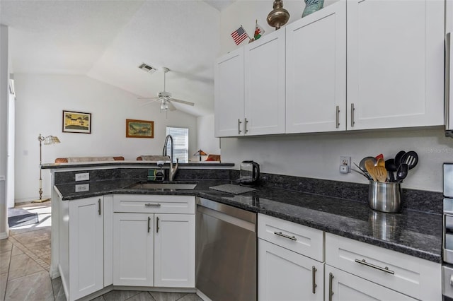 kitchen with lofted ceiling, white cabinetry, stainless steel dishwasher, dark stone countertops, and sink