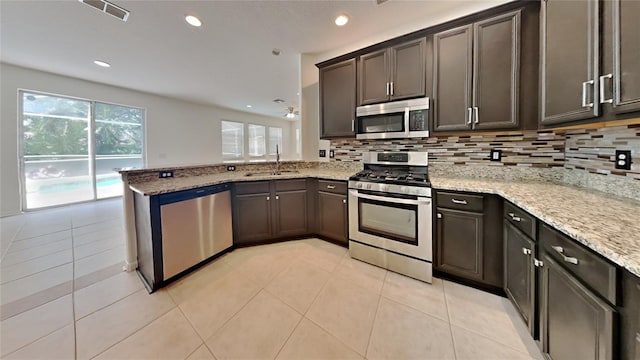 kitchen featuring appliances with stainless steel finishes, light stone counters, kitchen peninsula, and sink