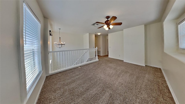 carpeted spare room featuring ceiling fan with notable chandelier