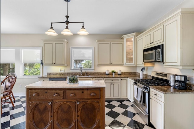 kitchen featuring cream cabinetry, light floors, appliances with stainless steel finishes, and glass insert cabinets