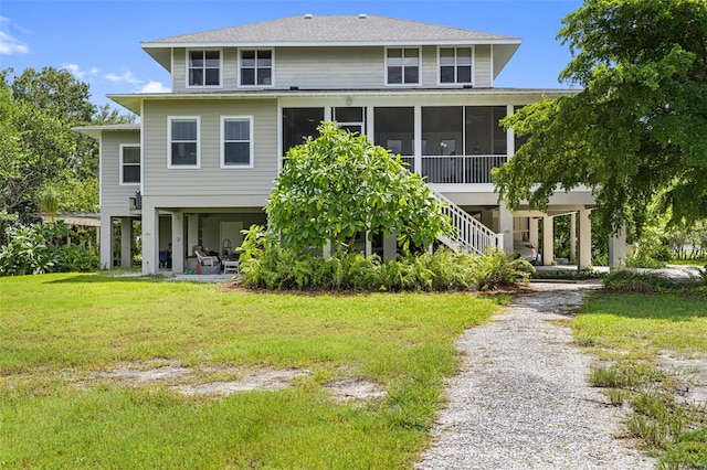 back of house with driveway, a sunroom, a carport, and a yard