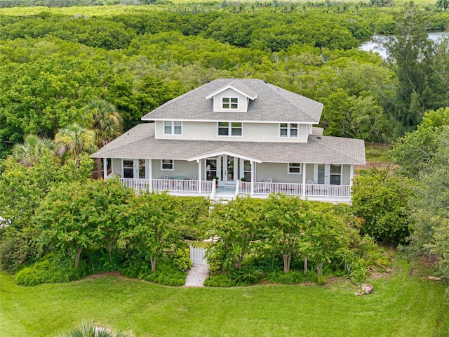 view of front of property featuring a front yard, roof with shingles, and a wooded view