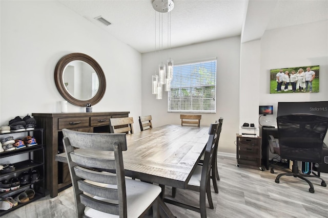 dining space with light hardwood / wood-style flooring, a notable chandelier, and a textured ceiling