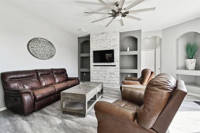 living room featuring a stone fireplace, ceiling fan, built in features, and light hardwood / wood-style flooring