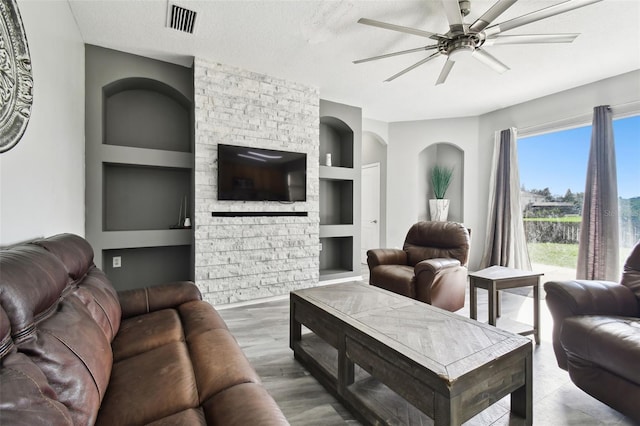 living room with built in shelves, a textured ceiling, a fireplace, and ceiling fan